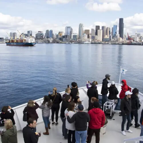 People on the deck of the Seattle Harbor Cruise take in the Seattle cityscape.